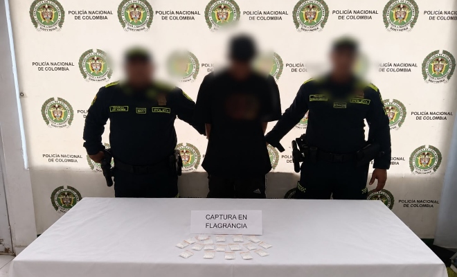 Dos funcionarios policiales con un ciudadano capturado frente a pendón institucional 