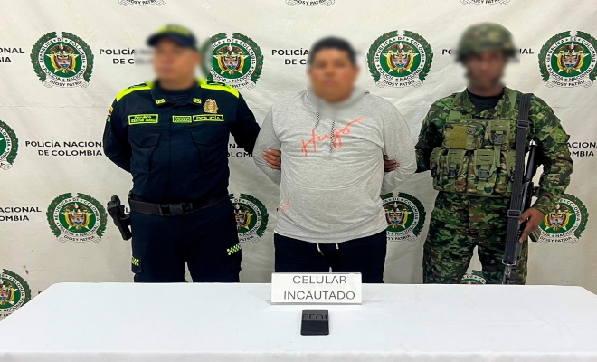 Funcionario policial y del Ejercito Nacional junto a un ciudadano capturado frente al pendón institucional 