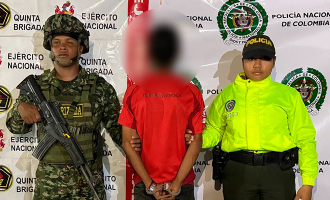 Persona capturada vestida con una camiseta color rojo siendo escoltado por funcionarios de la Polic&iacute;a Nacional y Ejercito de Colombia