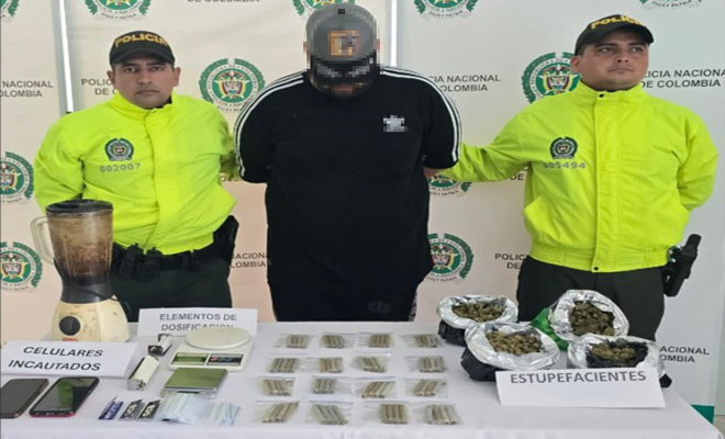 Se observa dos policías de la Sijin con un capturado y una mesa con marihuana , cigarrillo, dos celulares y elementos para dosificación de alucinógenos