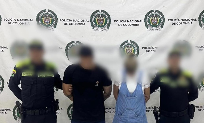 Dos funcionarios policiales con dos personas capturadas un hombre y una mujer frente al pendón institucional