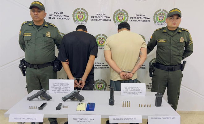dos polic&iacute;a con dos capturados  y una mesa con dos armas de fuego y  celulares