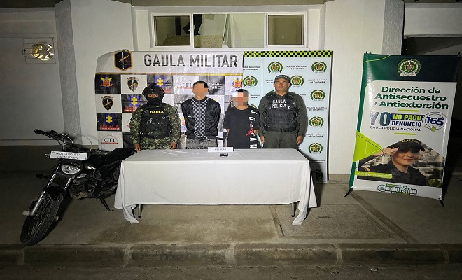 Fotografía de dos personas capturadas por el delito de extorsión, un funcionario del GAULA de la Policía Nacional y un funcionario del GAULA militar brindando seguridad 