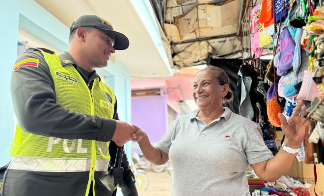 Un joven auxiliar de policía saludando a una ciudadana en sector comercial
