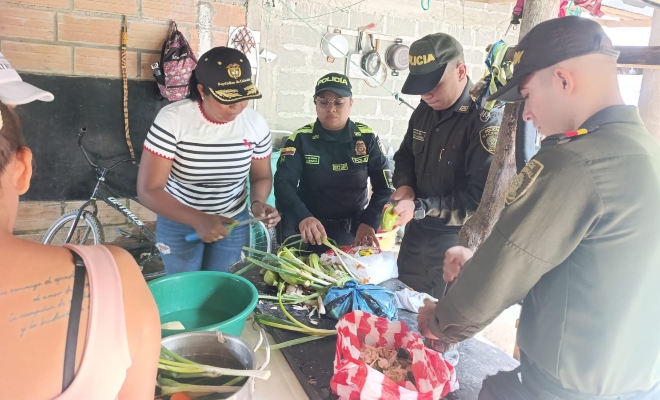 Tres funcionarios policiales junto a una ciudadana cocinando en actividad olla comunitaria