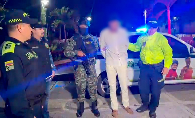 Persona vestida con buzo y pantalón blanco siendo conducido a la estación de policía 