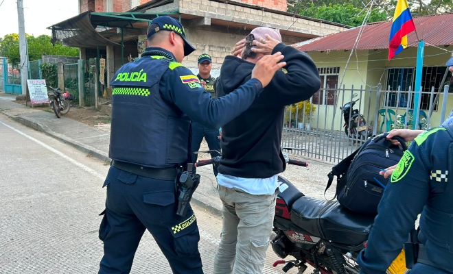 Dos funcionarios policiales realizando registro a persona a un ciudadano frente a una motocicleta 