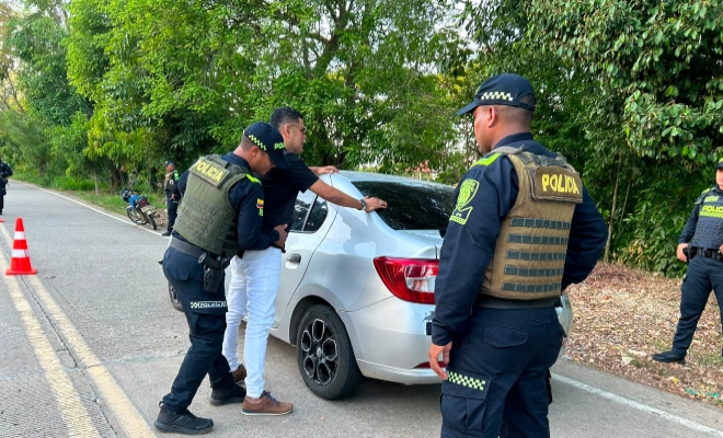 Tres funcionarios policiales realizando actividades de registro a persona a un ciudadano frente a un vehículo color gris