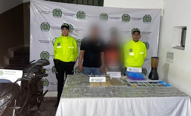 Dos policías custodiando dos capturados, una moto y estupefacientes