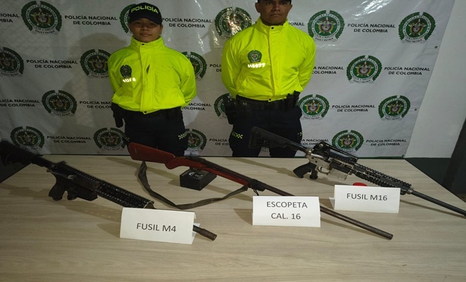 Dos uniformados, dos fusiles y una escopeta en una mesa