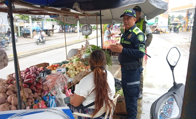 Un policia dando recomendaciones a una ciudadana y un policia prestando seguridad 