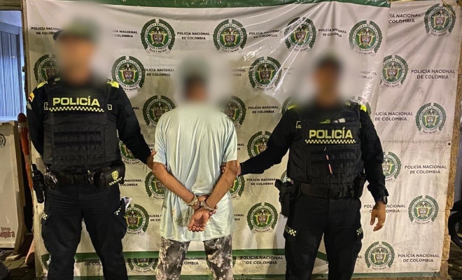 Dos funcionarios policiales con un ciudadano capturado frente a pendón institucional 