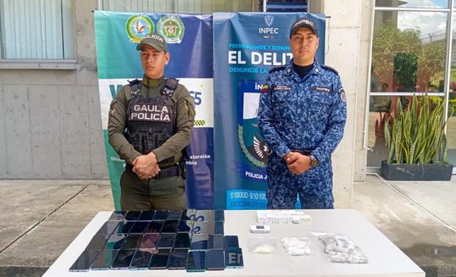 Funcionario del Gaula de la policia acompa&ntilde;ado de funcionario del Inpec y una mesa con celulares y cargadores