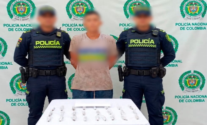 Dos funcionarios policiales junto a un ciudadano capturado frente a pendón institucional frente a ellos una mesa sobre la cual están las sustancias estupefacientes incautadas 