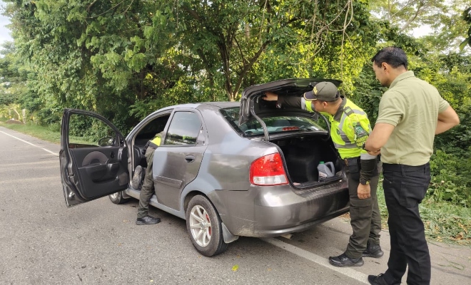 Funcionario policial de transito y transporte realizando registro a vehículo junto a un ciudadano 