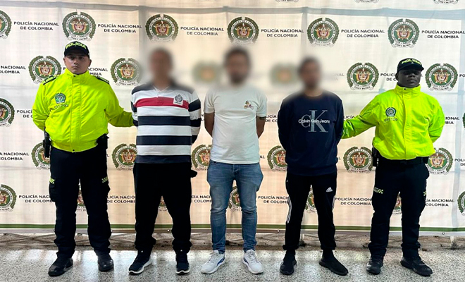 Dos polic&iacute;as sostienen tres capturados con fines de extradici&oacute;n.