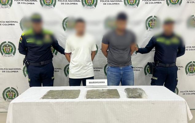 dos funcionarios policiales con dos ciudadanos capturados y frente a ellos una mesa con elementos estupefacientes incautados 