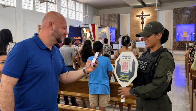 una funcionaria del grupo del GAULA de la Policía Nacional compartiendo a un ciudadano el código QR de las líneas de atención