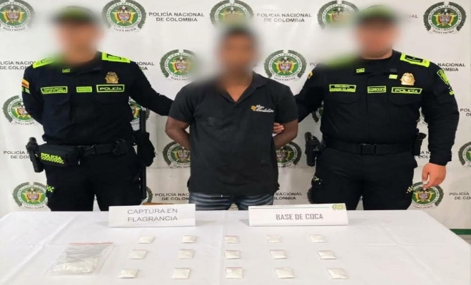 Dos funcionarios policiales con un ciudadano capturado frente a pendón institucional frente a ellos material incautado sobre una mesa