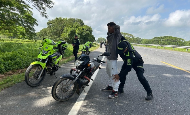 Funcionario policial realizando registro a persona a un ciudadano en la vía frente a una motocicleta