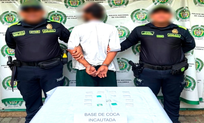 Dos funcionarios policiales con un ciudadano capturado frente a pend&oacute;n institucional frente a ellos material incautado sobre una mesa
