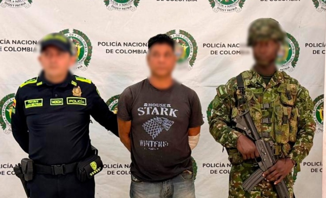 Funcionario policial y del Ejercito Nacional con un ciudadano capturado frente a pendón institucional 