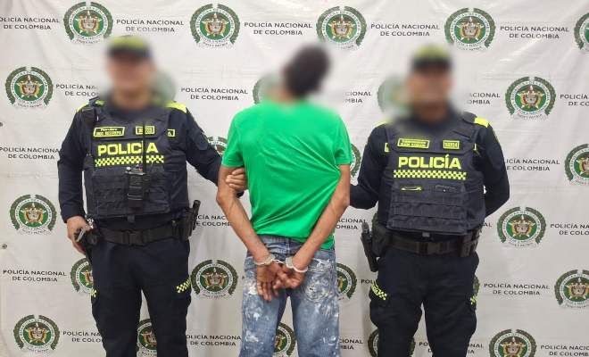 Dos funcionarios policiales con un ciudadano capturado frente a pendón institucional 