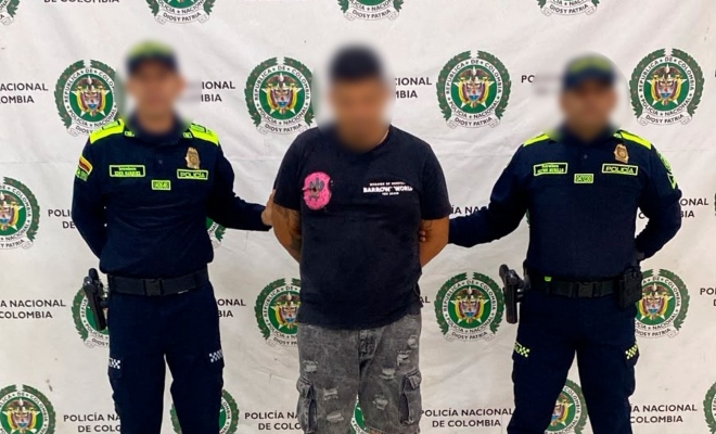 Dos funcionarios policiales con un ciudadano capturado frente a pendón institucional 