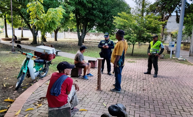 Dos funcionarios policiales realizando consulta de antecedentes a tres ciudadanos en un parque 