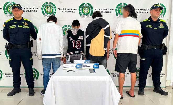 Cuatro hombres capturados en medio de dos Policías, en frente elementos recuperados
