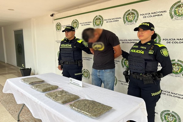 Dos policías junto a un capturado y una mesa con bolsas de estupefacientes