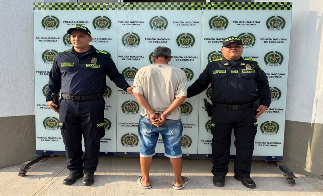 Una persona de sexo masculino de espaldas, capturado por el delito de Violencia Intrafamiliar, dos uniformados de la Policía Nacional brindando seguridad