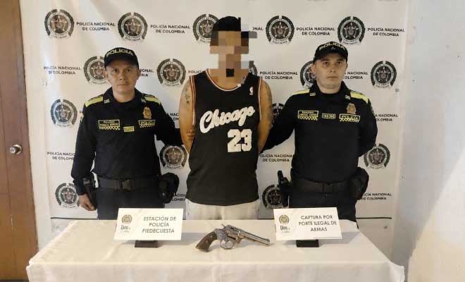 Hombre capturado en medio de dos Policías, en frente arma de fuego incautada