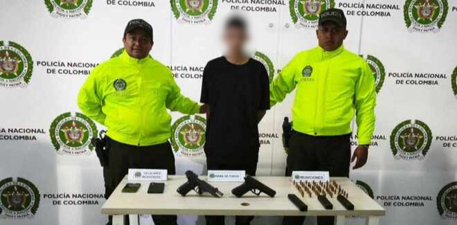 Persona capturada por la Policía Nacional con dos funcionarios, junto a armas y munición incautadas sobre una mesa.
