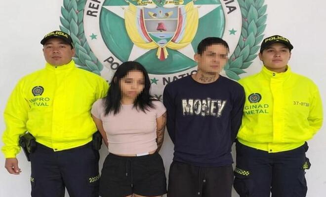 Cuatro personas de pie frente a un fondo institucional de la Polic&iacute;a Nacional de Colombia; dos personas en el centro y dos personas uniformadas a los lados.