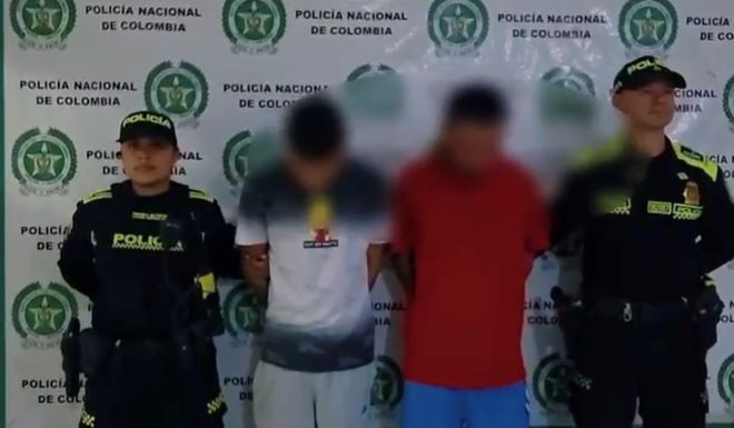 dos policías al lado de dos hombres capturados 