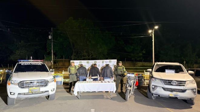 Dos polic&iacute;as al lado de dos hombre capturados con estupefacientes, un moto y una camioneta