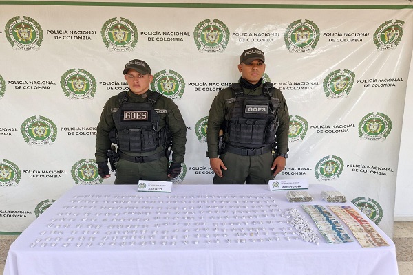 Dos policías junto a una mesa con sustancias estupefacientes y dinero en efectivo incautados