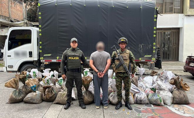Un hombre capturado con dos policías en cada lado y al fondo el vehículo y los insumos incautados 
