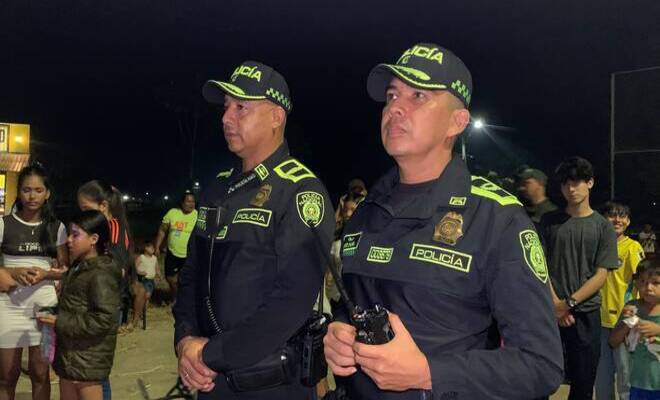 Dos oficiales de la Policía permanecen atentos y presentes durante una actividad pública nocturna, garantizando la seguridad de los asistentes y el desarrollo tranquilo del encuentro