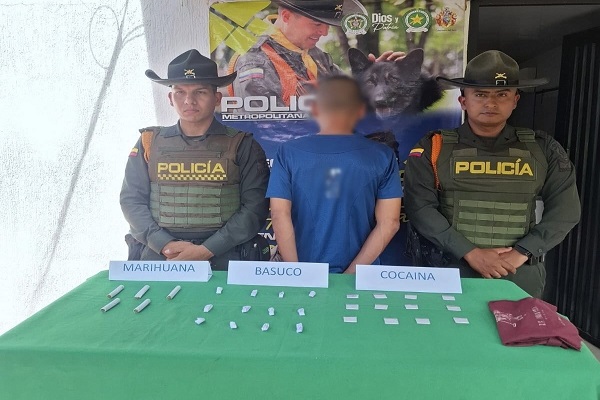 Dos funcionarios custodian a un ciudadano capturado junto a una mesa con estupefacientes