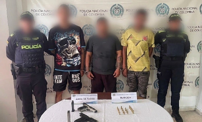Dos Policía custodian a tres individuos, presentado junto con el material bélico incautado.